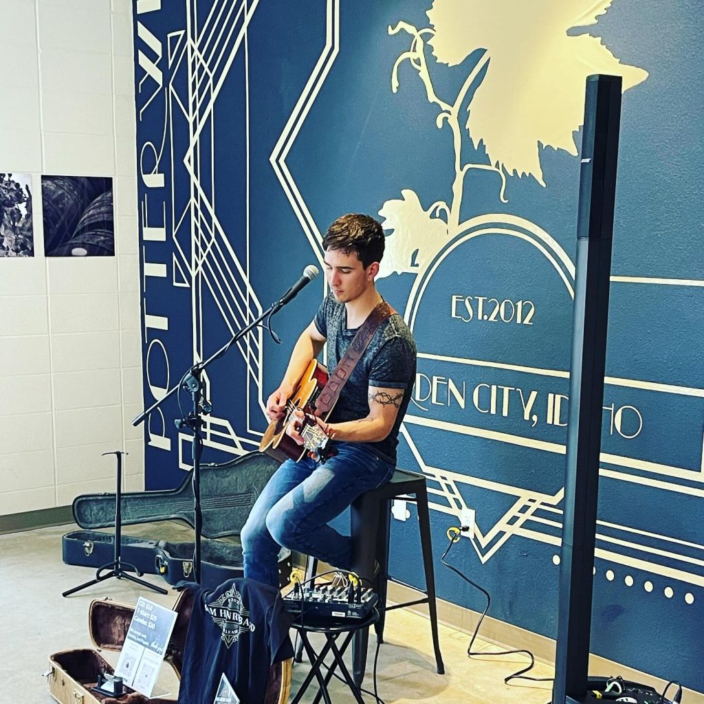 Young man on a stool playing guitar on stage at Potter Wines.