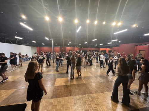 People country line dancing in a large, brightly lit room with wood flooring.