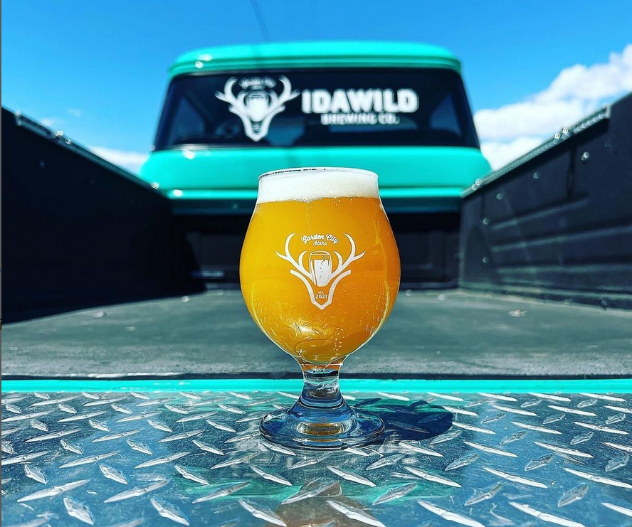 orange creamy looking liquid in a tulip glass with a white stag image on it on a truck tailgate